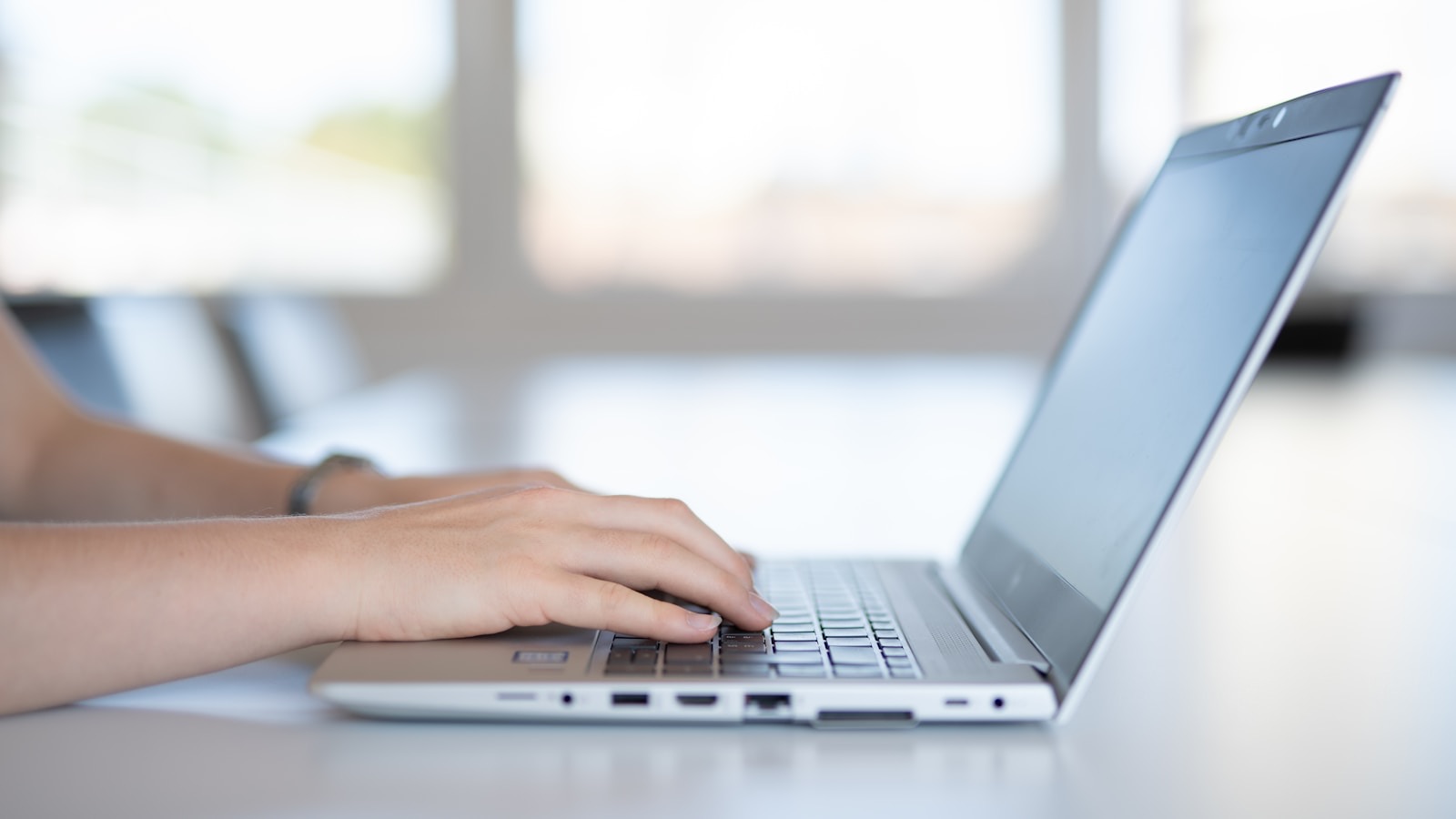 Hands typing on a laptop at a bright workspace