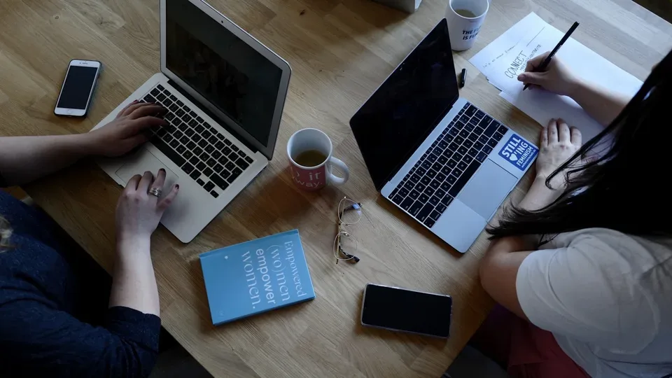 Zwei Kolleginnen arbeiten gemeinsam mit Laptops an einem Tisch